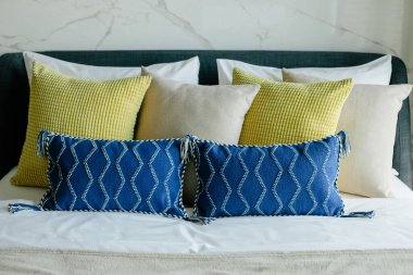 Yatakta farklı renk ve boyutlarda yastıklar düzgünce dizilmiş. İç tasarım..