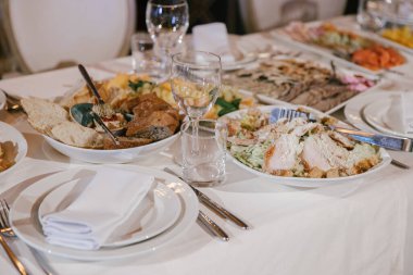 Ziyafet ya da kutlama için masa hazırlamak. Alkollü içecekler, şarap ve meyve suyu için boş bardaklar, beyaz tabakta bez peçeteler ve masada çatal bıçak. Soğuk mezeler ve salatalar..