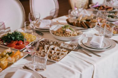 Ziyafet ya da kutlama için masa hazırlamak. Alkollü içecekler, şarap ve meyve suyu için boş bardaklar, beyaz tabakta bez peçeteler ve masada çatal bıçak. Soğuk mezeler ve salatalar..
