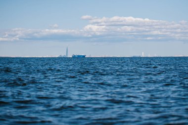 Finlandiya Körfezi 'nin bir yaz günü sularından bakıldığında, kargo gemileri ve gemileri uzaklarda, mavi sularda ve büyük dalgalarda yüzüyor. St. Petersburg kıyıları. Rusya, Peterhof, 31.07.2021