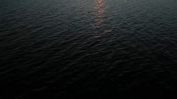 Luchtfoto van een drone die bij zonsondergang over het zee- of oceaanoppervlak vliegt, de reflectie van de oranje zon in het water.Golven en licht met schittering op het wateroppervlak.Hemelse achtergrond — Stockvideo