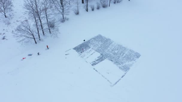 Letecký pohled na zamrzlý rybník v zimě, lidé čistí led ze sněhu s velkou lopatou pro bruslení, zimní kluziště — Stock video