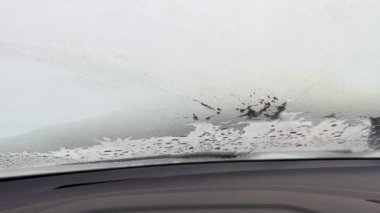 Arabanın içine, donmuş ön cama bak. Arabanın camında eriyen buz. Eriyen karın dokusu yakın plan, ön camda kış desenleri.