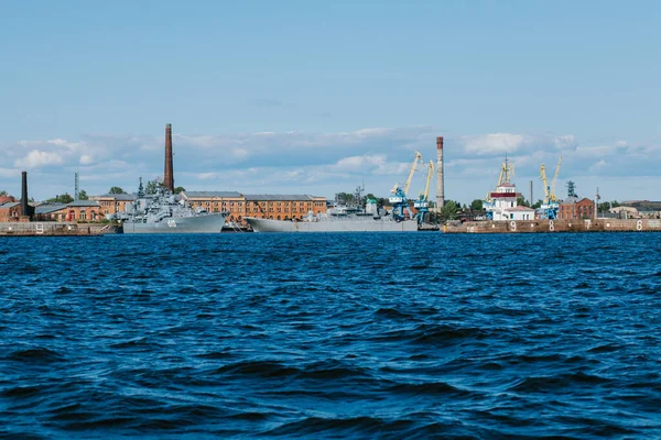 Вид з води на узбережжя Кронштадту, де є військові кораблі і кораблі, морські крани на платформі, блакитна вода і великі хвилі. Росія, Кронштадт, 31.07.2021 — стокове фото