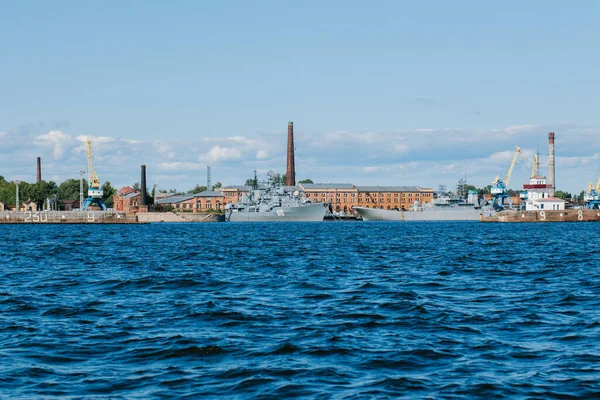 Uitzicht vanaf het water naar de kustlijn van Kronstadt, waar oorlogsschepen en schepen, zeekranen op het platform, blauw water en grote golven zijn.Rusland, Kronstadt, 31.07.2021 — Stockfoto