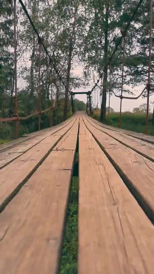 Vieille passerelle étroite en bois suspendue au-dessus d'une petite rivière. Gros plan — Video