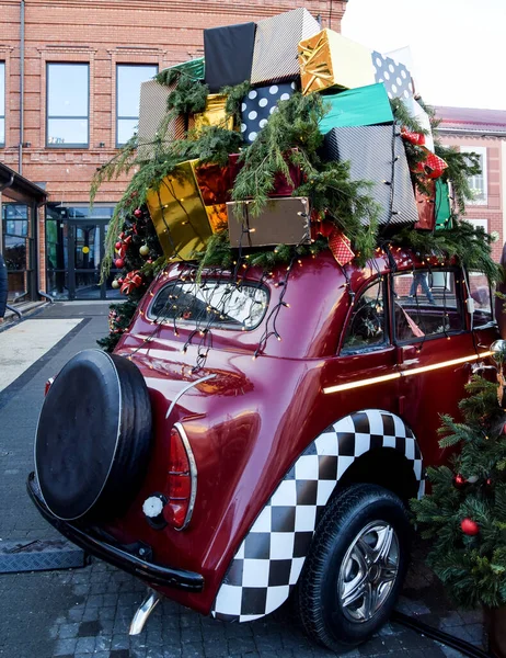 许多礼品盒放在一辆红色复古汽车的车顶上 他们正被送往度假 圣诞树上装饰着玩具 还有一辆装有礼物的汽车 图库照片