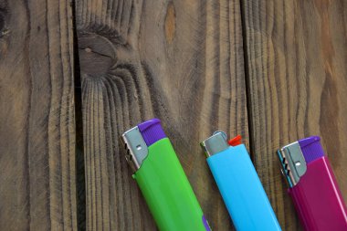 Ahşap arka planda üç tane çok renkli çakmak. Gaz çakmakları mavi, yeşil ve kırmızı sağ tarafta ve mesaj için bolca yer var..