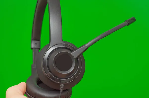 緑の背景でオンラインで作業するためのマイク付きの黒いヘッドセット — ストック写真