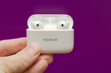 Rusya, Irkutsk Bölgesi, 17 Şubat 2022: Bir adamın elinde beyaz kablosuz kulaklıklar var. Mor arka plandaki bir suçlama davasında Honor Earbuds 2 Lite.