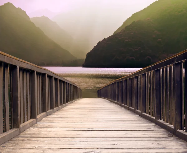 Mountain lake and flowing river with a wooden bridge — Stock Photo, Image