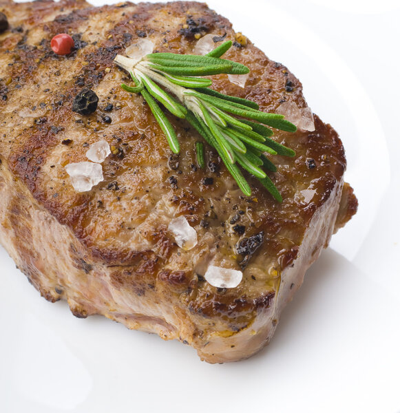 Beef steak with rosemary and spices on white plate on wooden table