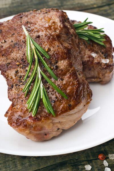 Beef steak with rosemary and spices on white plate on wooden table