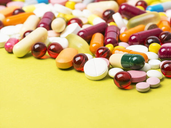 Colorful pills and capsules on yellow background