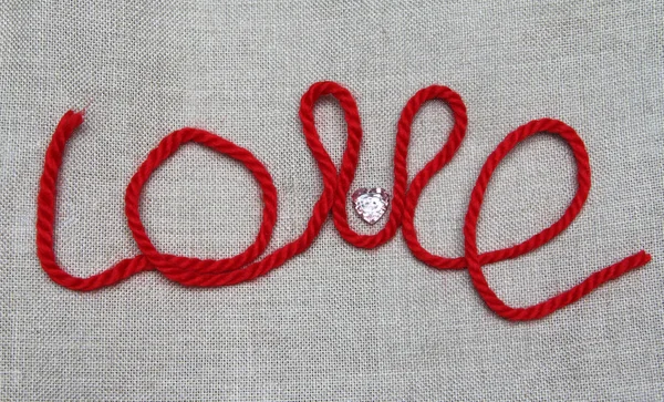 Word "love" from red thread and a button in the form of heart — Stock Photo, Image