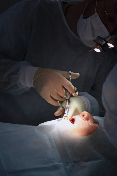 Der Zahnarzt spritzt während der Operation eine Spritze. Zahnimplantation Chirurgie. Mund auf. Ein älterer Patient. Vertikales Foto. Moderne Zahnmedizin. — Stockfoto