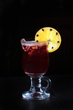 Geleneksel kırmızı şarap, meyve ve baharat kokteyli. Siyah arka planda cam bir bardakta sıcak şarap. Sıcak, sağlıklı bir içecek. Dikey fotoğraf. Yan görünüm.