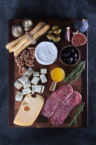 Several types of cheeses on a wooden board with smoked sausage and olives. Figs and grissini on board. Serving board. Flat lay. Stock Photo