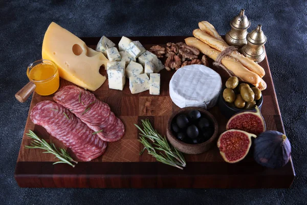 Several types of cheeses on a wooden board with smoked sausage and olives. Figs and grissini on board. Serving board. Selective focus. Stock Image