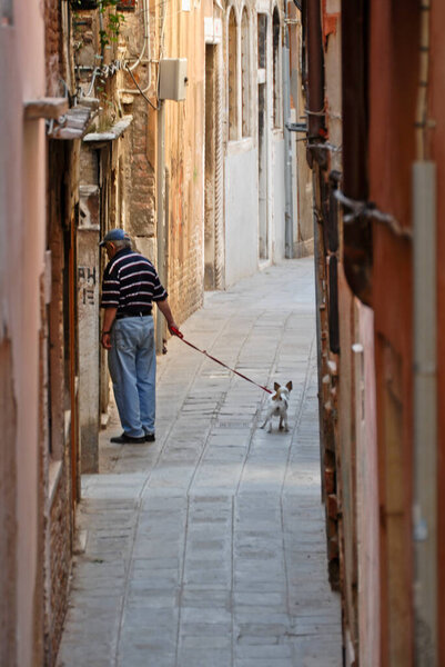An unrecognizable man walks with his dog through the city of Venice, Italy.