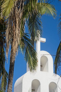 Mavi gökyüzüne karşı modern Hıristiyan kilisesinin beyaz arması ve her yerde palmiye yaprakları. Playa del Carmen, Meksika