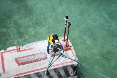 Liman işçisi, limandaki bir rıhtımda bir demirleme kordonuna bağlanmış bir gemiyi çekiyor..