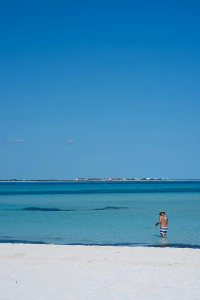 Denizde mayo giymiş bir adam ufukta ve mavi gökyüzünde görünüyor.