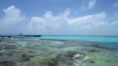 Meksika 'nın Mujeres Adası' ndaki kayalık kıyı şeridi ve berrak deniz. Arka planda turist tekneleri bağlamak için ahşap bir iskele var..