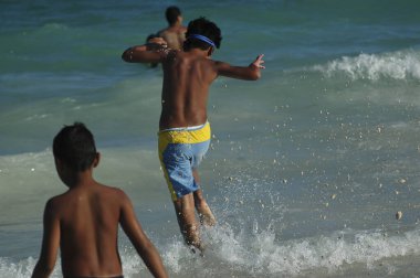 Rear view in a young Mexican running into the sea, and jumping over the waves. Selective focus