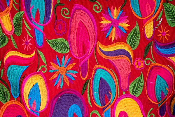 Colorful handmade fabric from Chiapas, Mexico. Flowers edged in various colors on a red background.