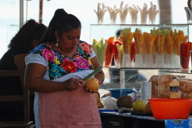 Close-up of a fresh exotic Mexican fruit vendor while she is cutting a grapefruit: In the background burgundy packs of mixed fruit
