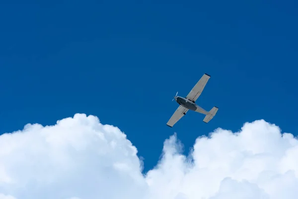 Small plane flying against blue sky and white sunlit clouds in Mexico