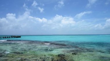 The coastline and crystal clear sea of Isla Mujeres, Mexico. In the background is a wooden pier for docking tourist boats.