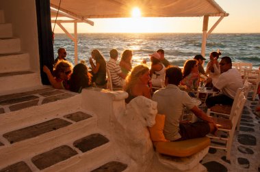 Yunanistan 'ın Mykonos adasında gün batımını izleyen bir grup turist barda oturuyor.