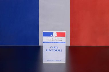Karanlık bir masaya yerleştirilmiş bir Fransız oy kartı broşürü. Arka planda üç renkli bir Fransız bayrağı. Boşluğu kopyala.