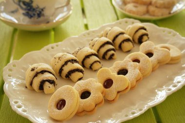 Samur ekmek ve haşhaş tohumu dolu bir pasta tabağı. Fincan ve fincan tabağı arka planda. Yeşil masa.