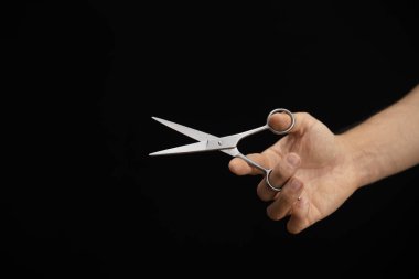 Sağ taraftan siyah bir zeminde elinde makasla gelen bir adamın eli.