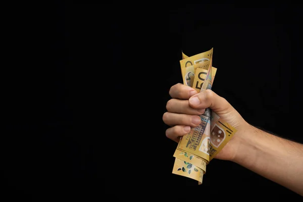 hand of a man squeezing australian dollars on a plain black background coming from right side