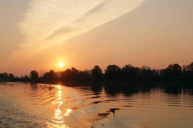 Manzara nehirde güzel bir gün batımı, ve suda teknenin izleri.