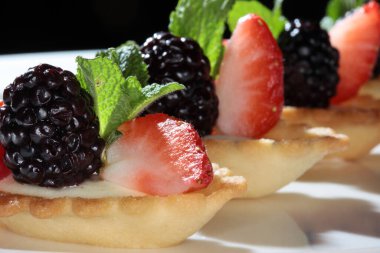 Koyu bir arka plan stüdyosunda çilek ve böğürtlenli lezzetli bir pasta.