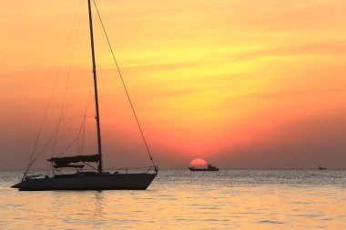 Deniz manzaralı gün batımı ve Tayland kıyılarında sönük yelkenli bir tekne.
