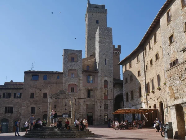 中央に八角形の井戸とその背後に中世の高い塔を持つサン ジミニャーノのシスタント広場 — ストック写真