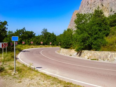 Asfalt yol yüksek dağlarda sahil boyunca bir gezi, bir yol hız göstergesi ve sarp kayalıklar üzerinde yeşil yılan