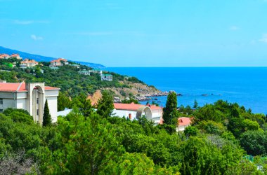 Güneşli bir tatil köyü ve yemyeşil otelin penceresinden bir manzara ve deniz kıyısına yakın evler.