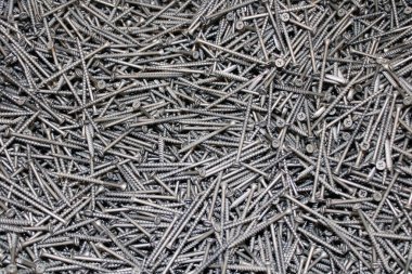 Kendi kendine dokunan vidaların dokusu arka plandaki metalik gümüş renkli çivileri bir ev inşaatında satışa sunuyor.