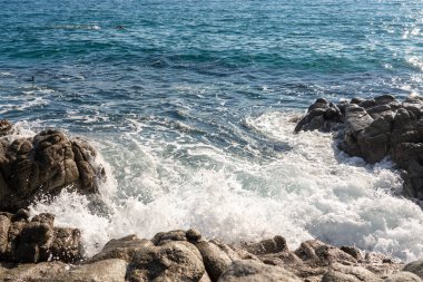 Dalgalar deniz kıyısındaki kayalara vuruyor, oldukça sakin bir deniz.
