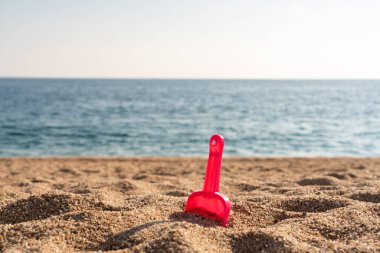 Kırmızı oyuncak kürek kumsalda kumsalda, arkasında deniz ya da okyanus olan.
