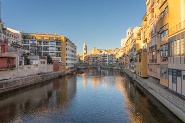 Girona, İspanya - 12.20.2021: Girona 'nın tarihi merkezinde renkli evler ve açık gökyüzü ile Eiffel Köprüsü manzaralı nehir kanalı