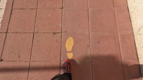 スニーカー姿の男が街の黄色い塗装済み歩道を進み — ストック動画