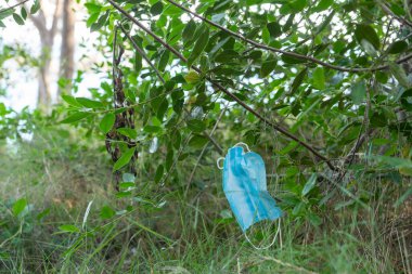 Ormanda bir çalılıkta asılı duran mavi bir tıbbi maske, doğa için covid 'in sonuçları.